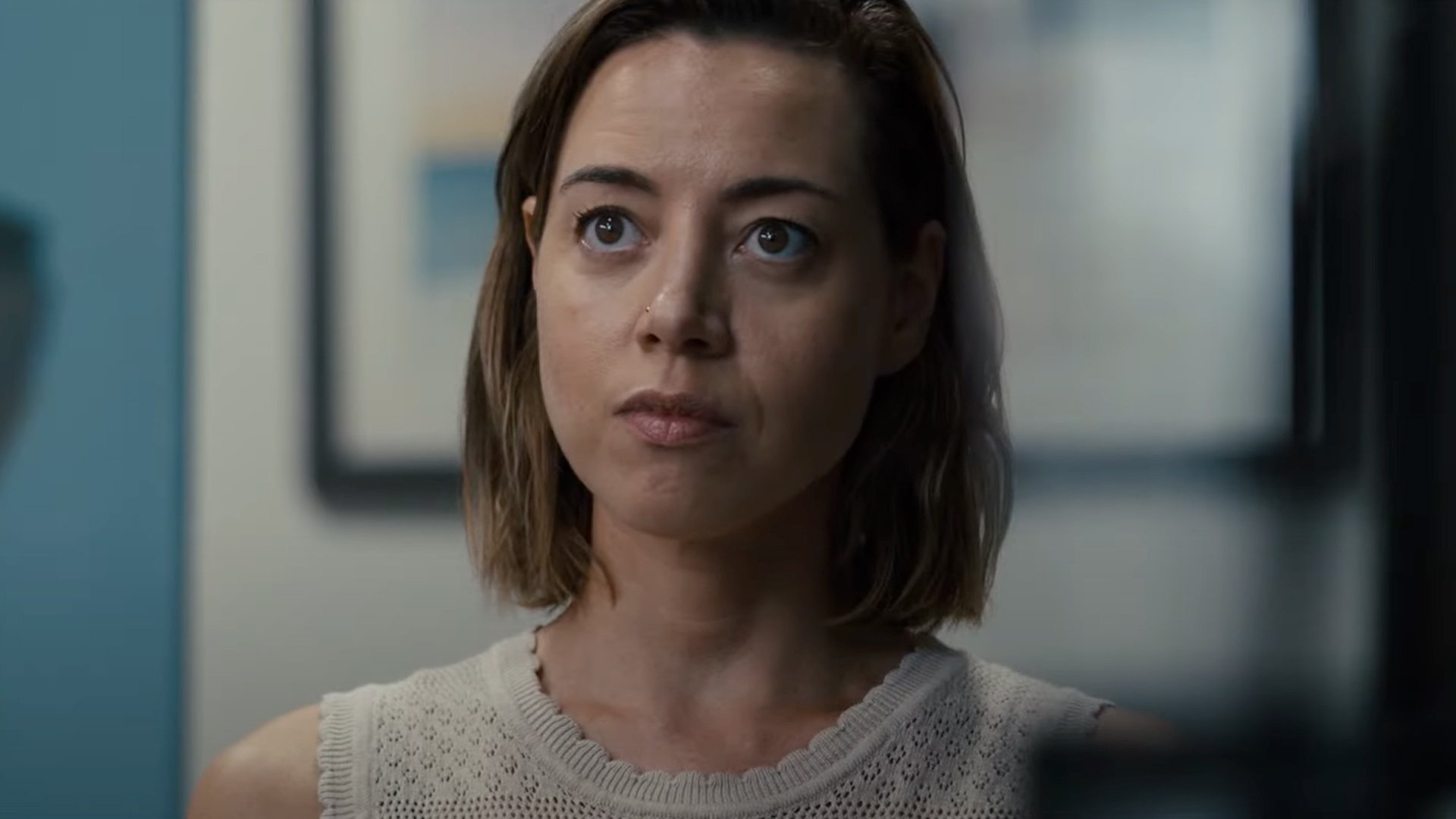 A young woman with short hair in a tank top stares at someone out of frame.