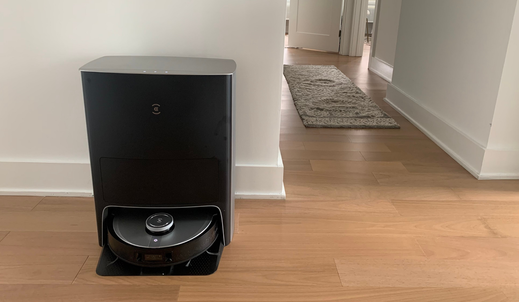 Ecovacs Deebot X1 Omni and station on wooden floor with hallway and rug in background