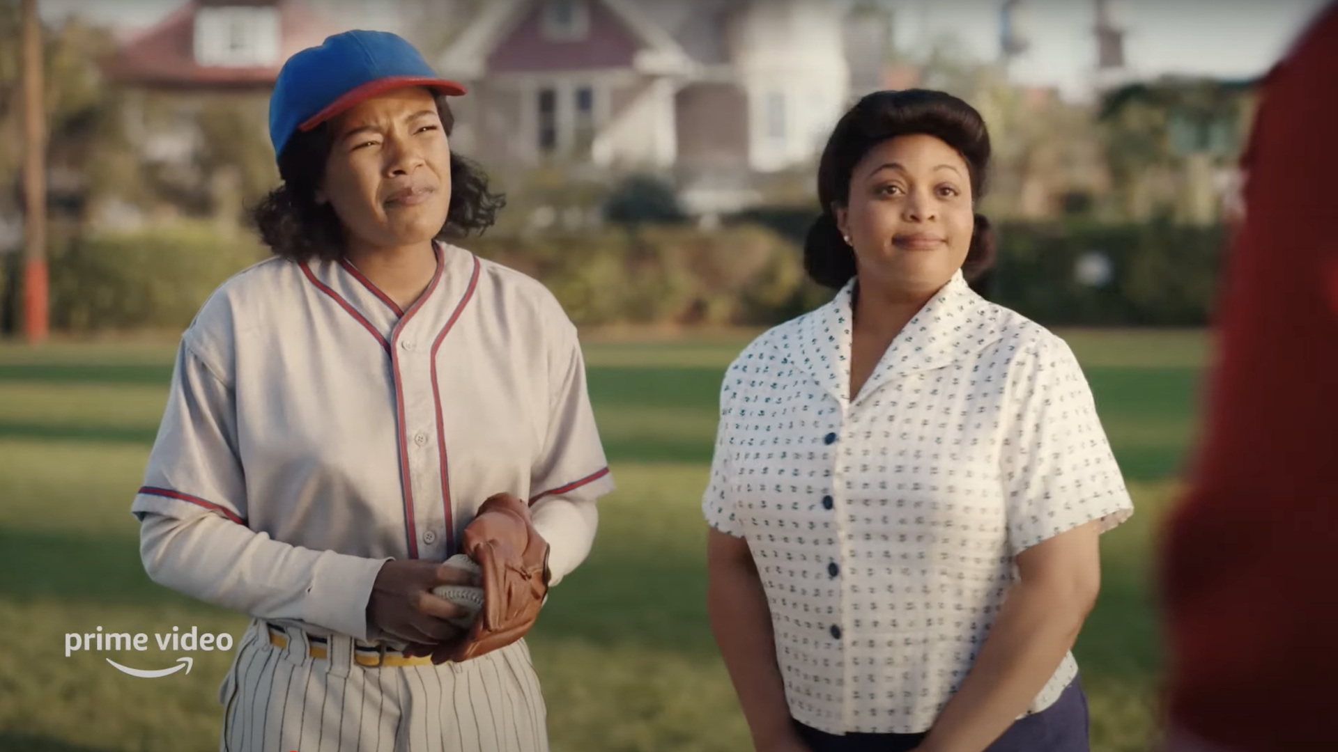 Two women stand on a baseball pitch, one holding a baseball.