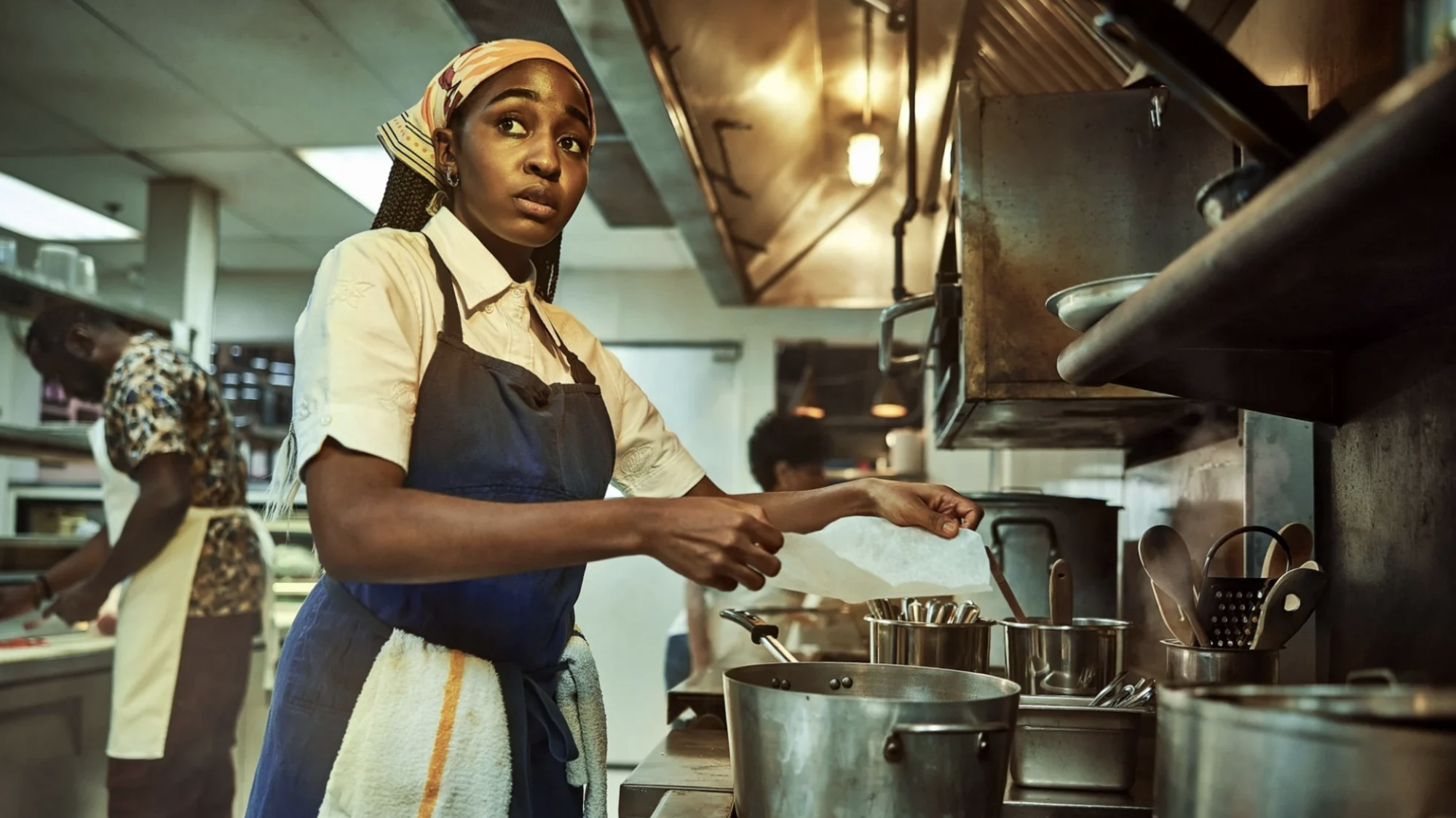 A woman wearing chef's clothes stands in a restaurant kitchen.