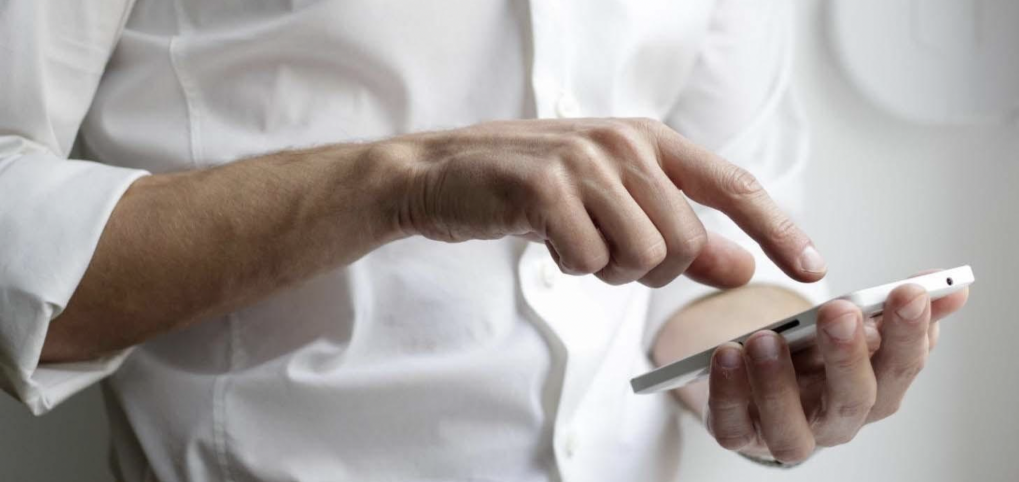 Person wearing white shirt holding tapping smart phone.