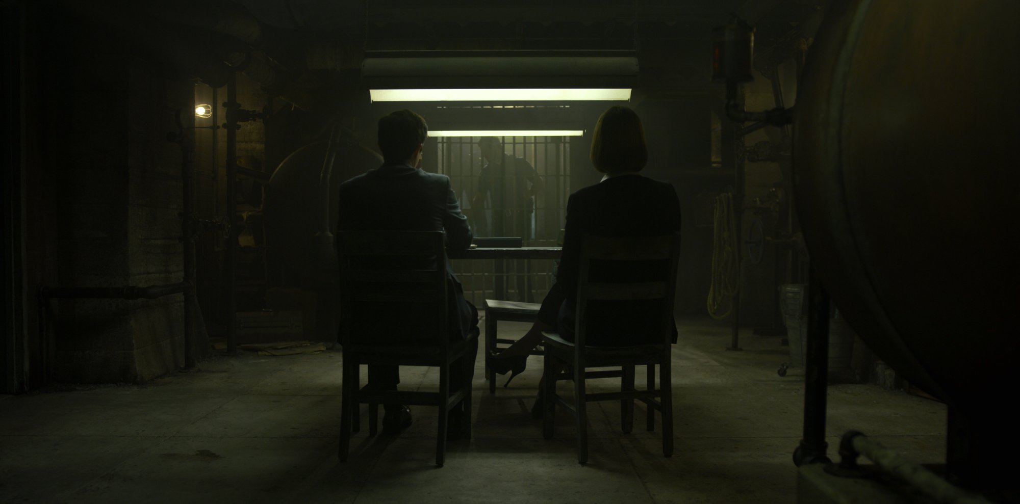Detectives sit at an interrogation table.