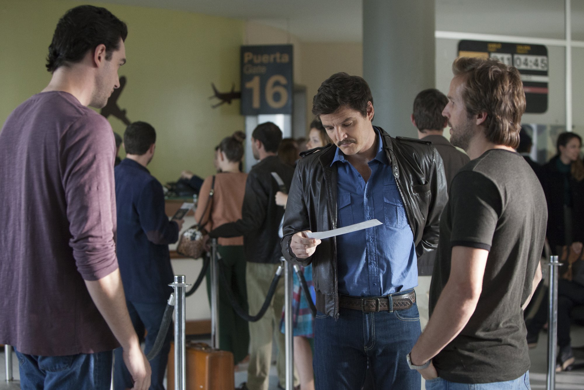 Three men stand around with each other, one looks at a piece of paper.