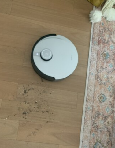 Robot vacuum on hardwood floor by pile of soil