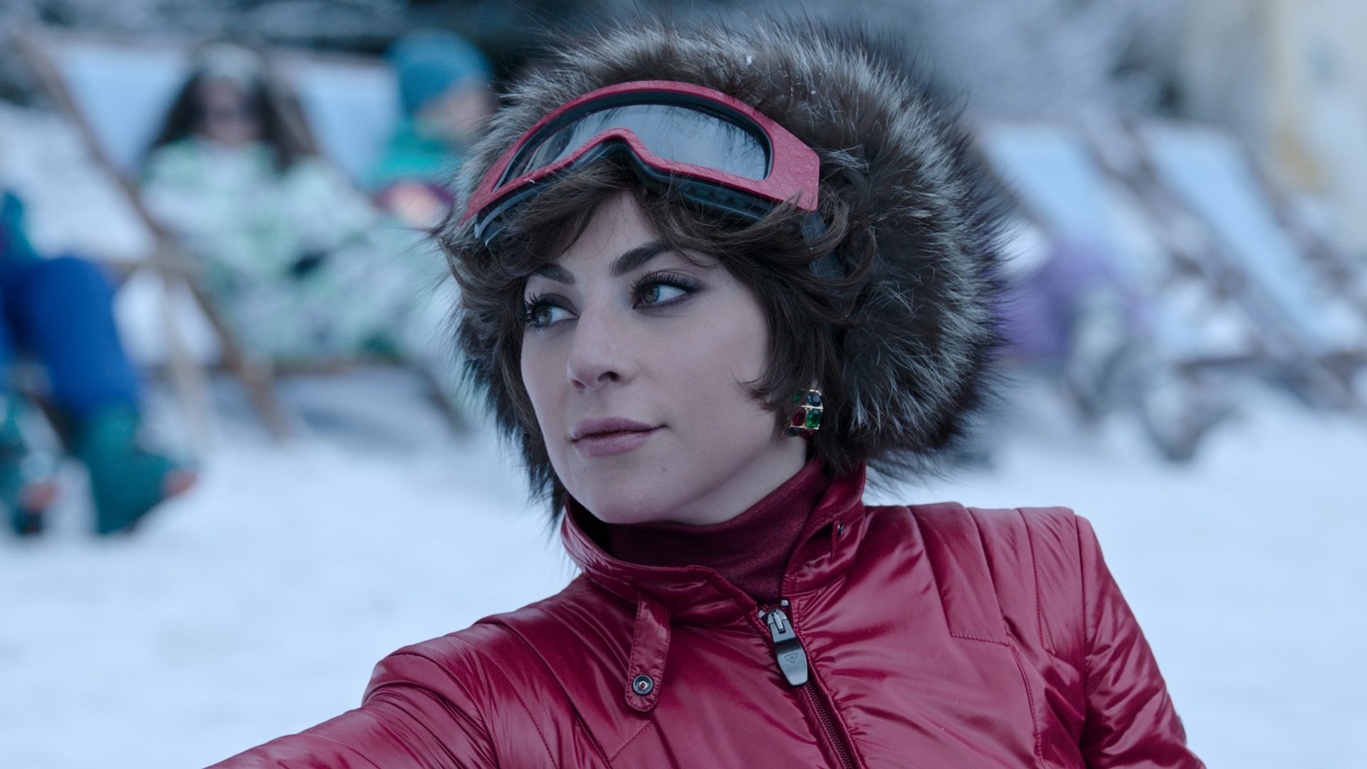 A woman dressed in fashionable ski wear sits on a deckchair in the snow.