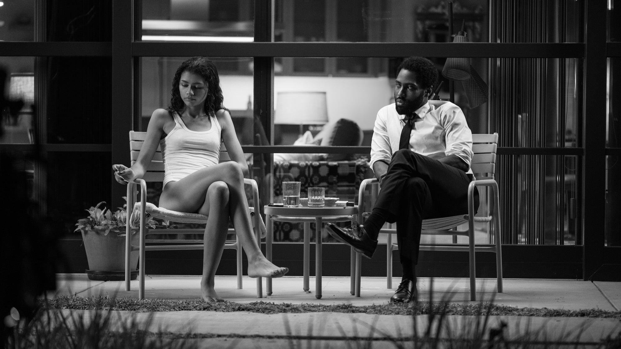 A couple sit outside their house on chairs late at night.