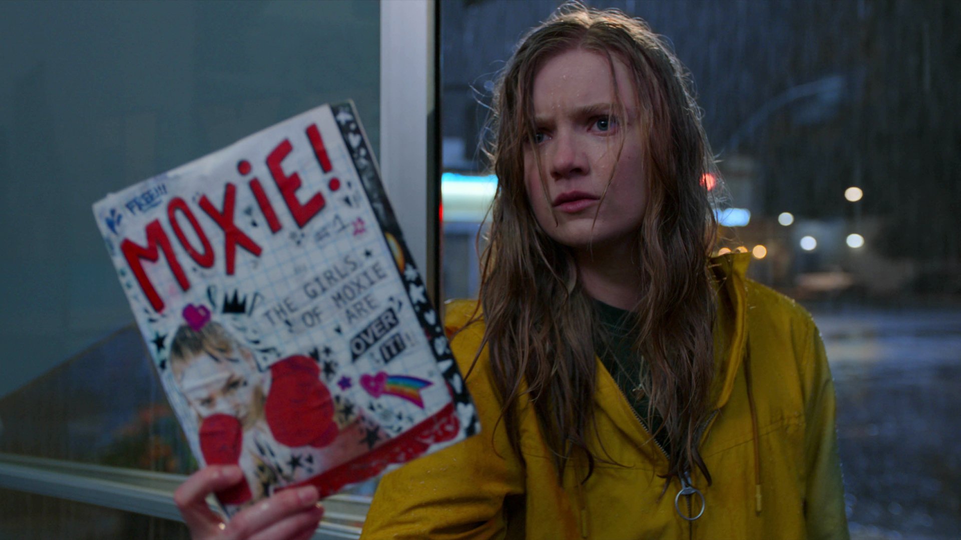 A girl holds up a zine called "Moxie!"