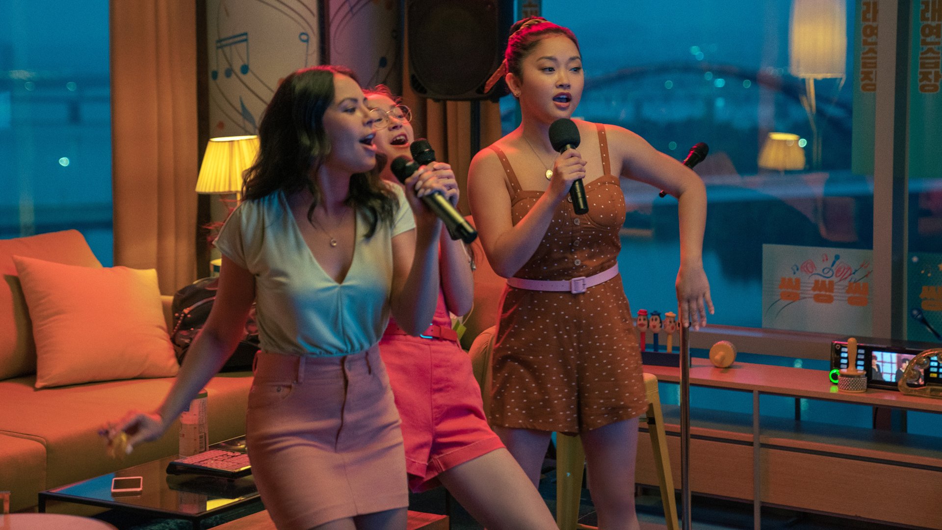 Three girls sing into microphones in a hotel room.