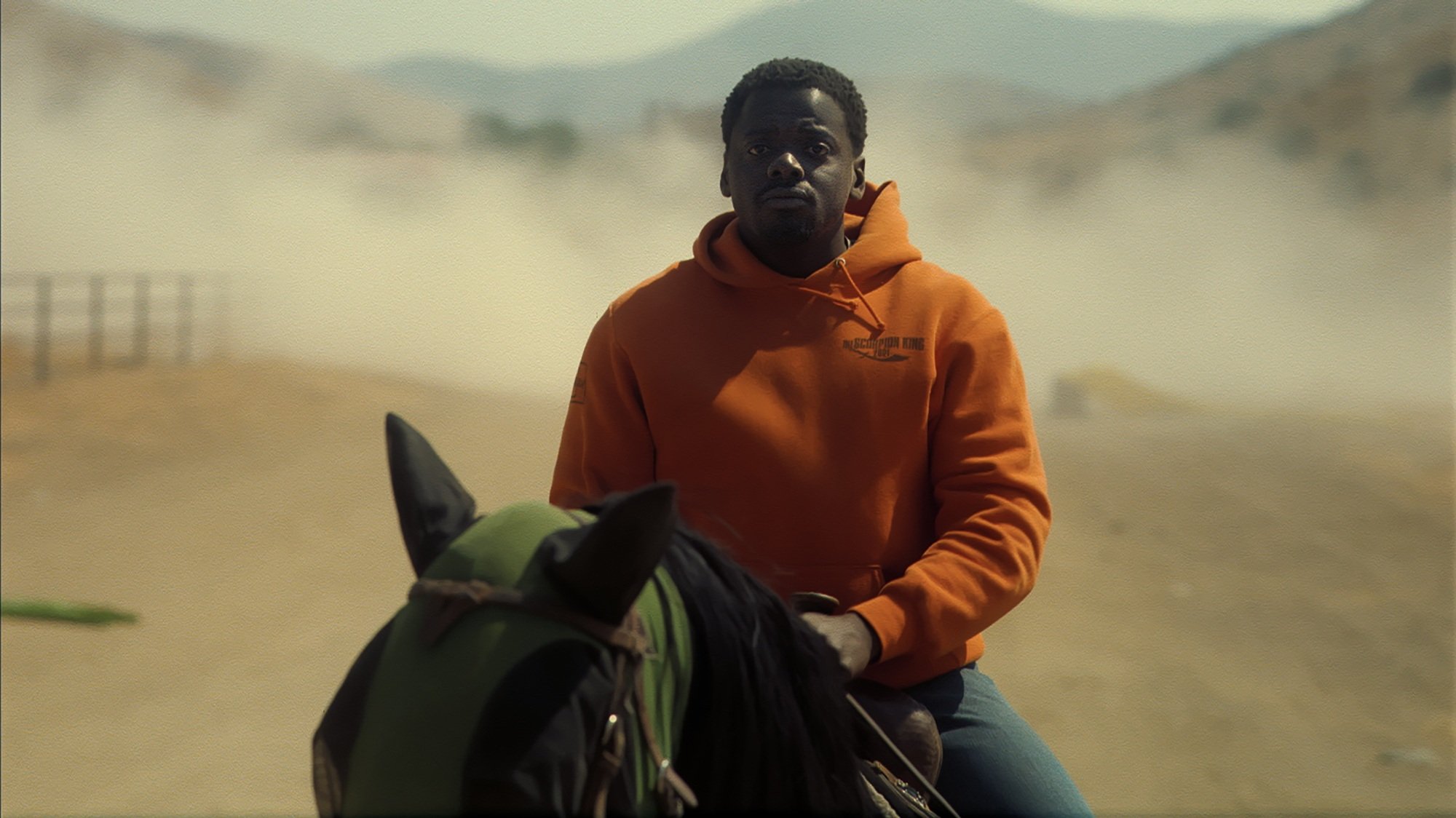 A man in an orange sweatshirt rides a horse on a dirt road