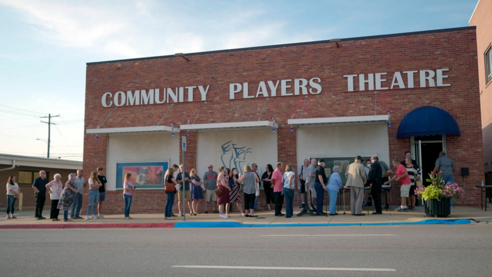 Nebraska Community Players Theatre exterior, with a line of audience members wrapping around the block. 