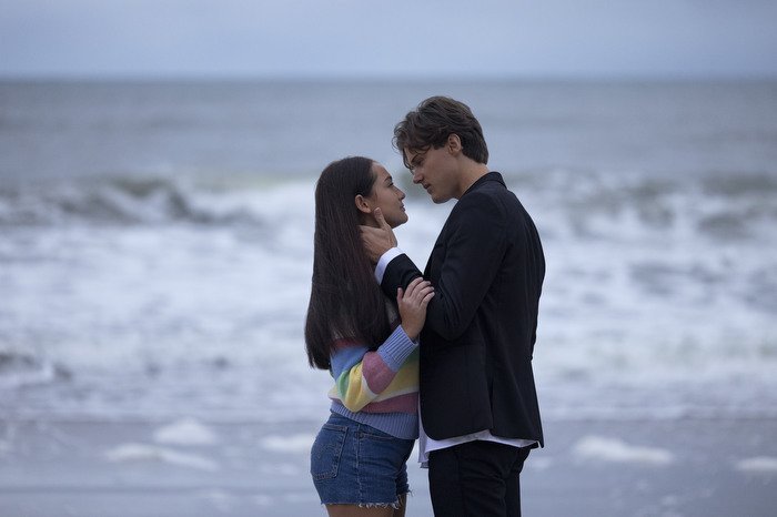 Two people look about to kiss on a beach.