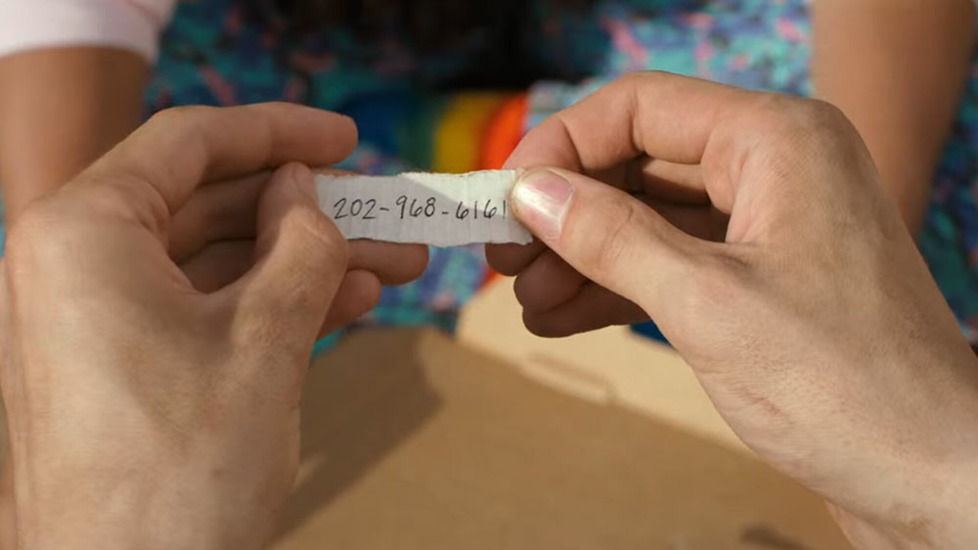 A person holds a slip of paper that shows a phone number.
