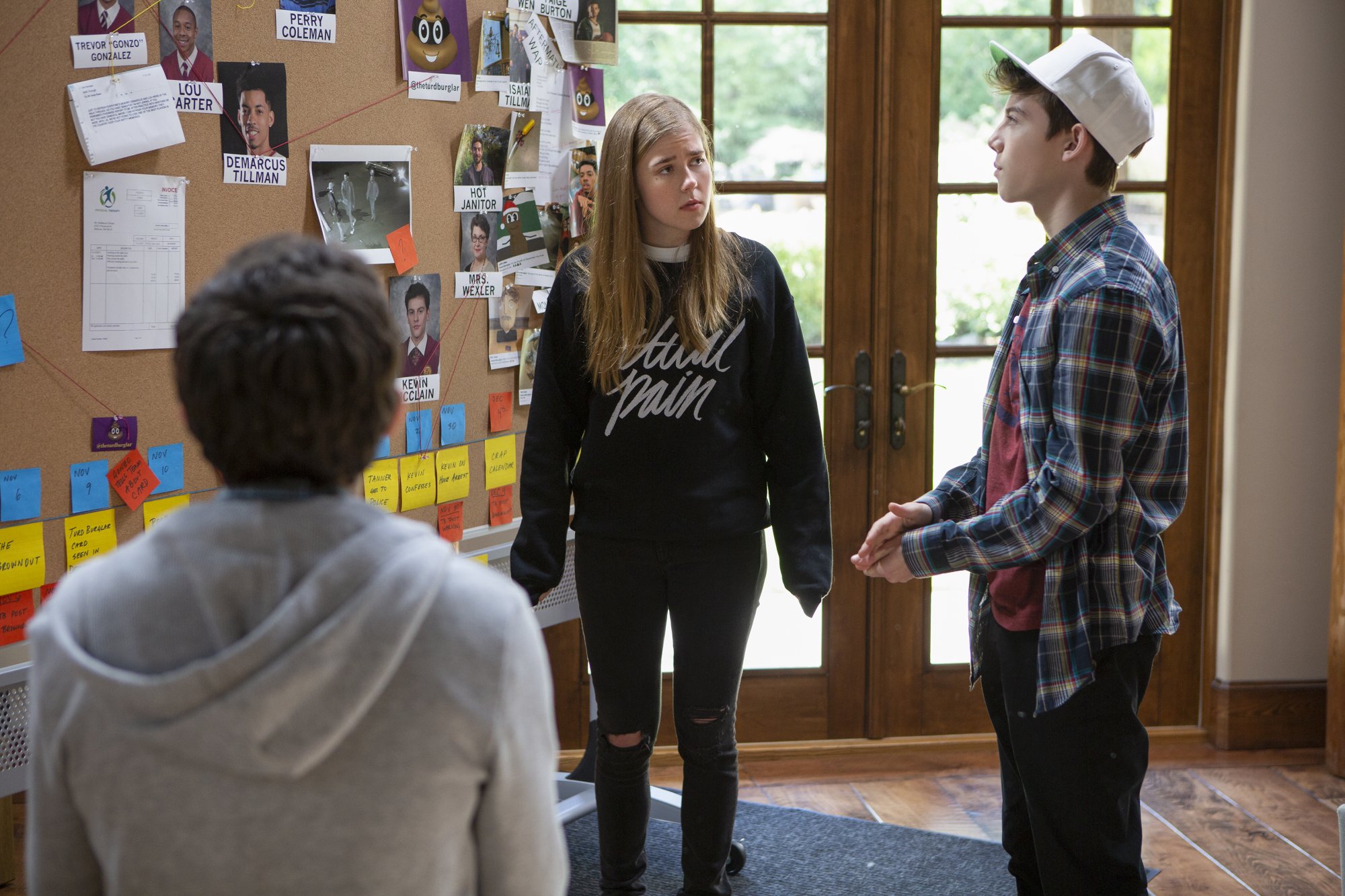 Three people stand around a board covered in clues.