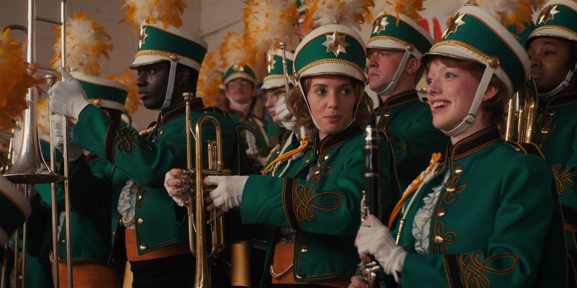 A high school band dressed in green and gold in a high school gym.