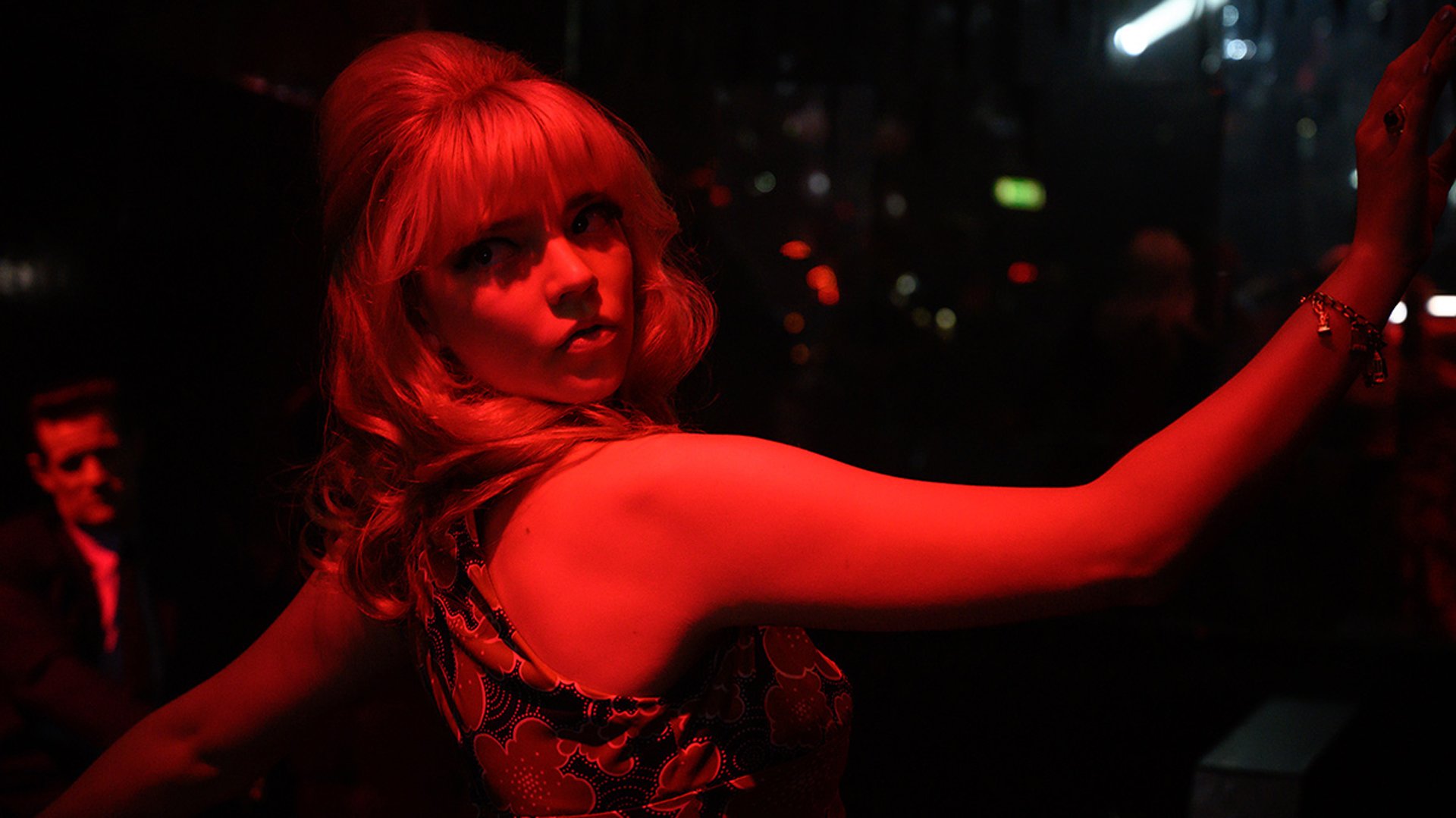 A young woman in 1960s dress dances beneath a red light.