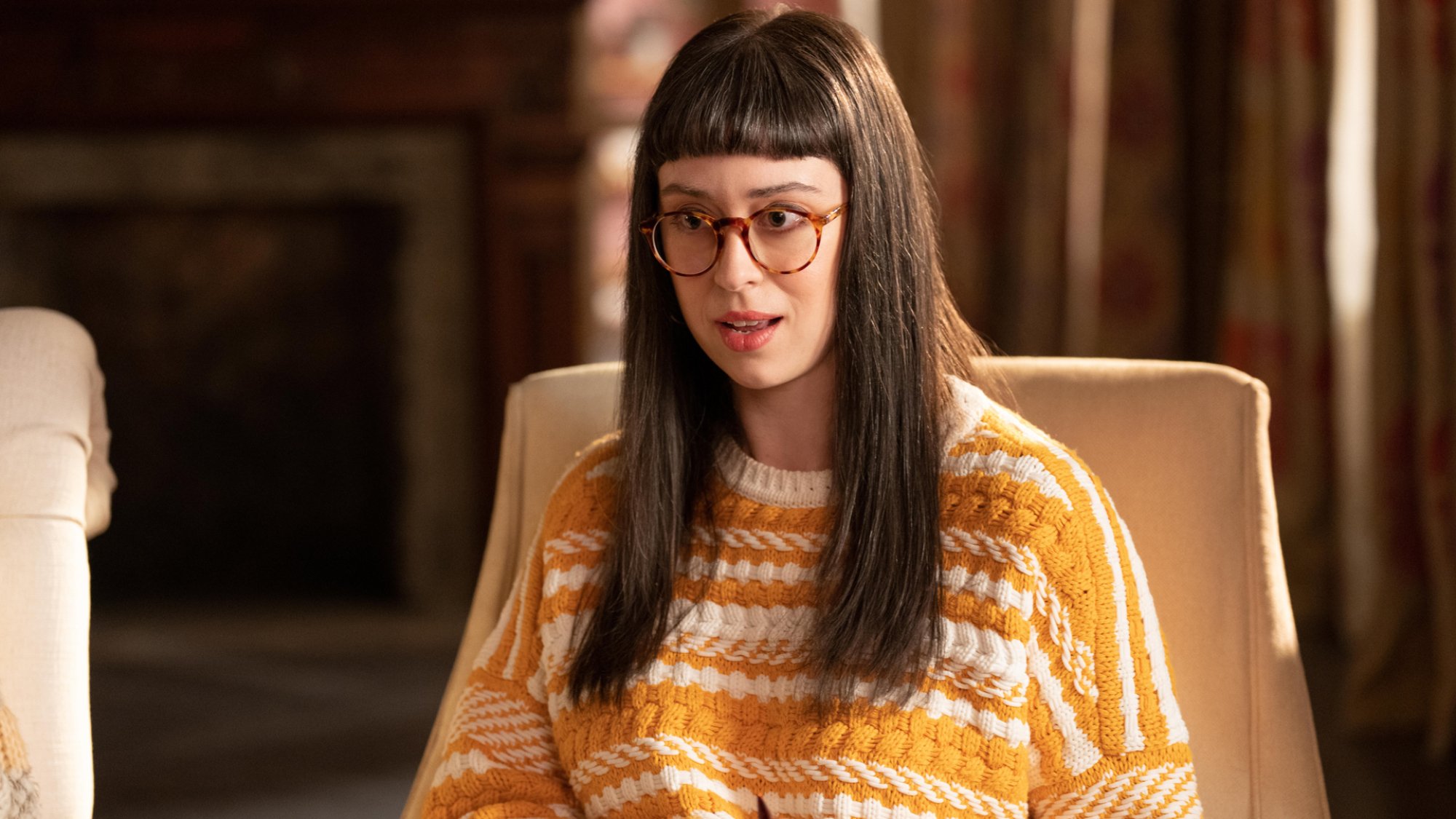 A woman with glasses wears a yellow striped sweater sitting in. chair.