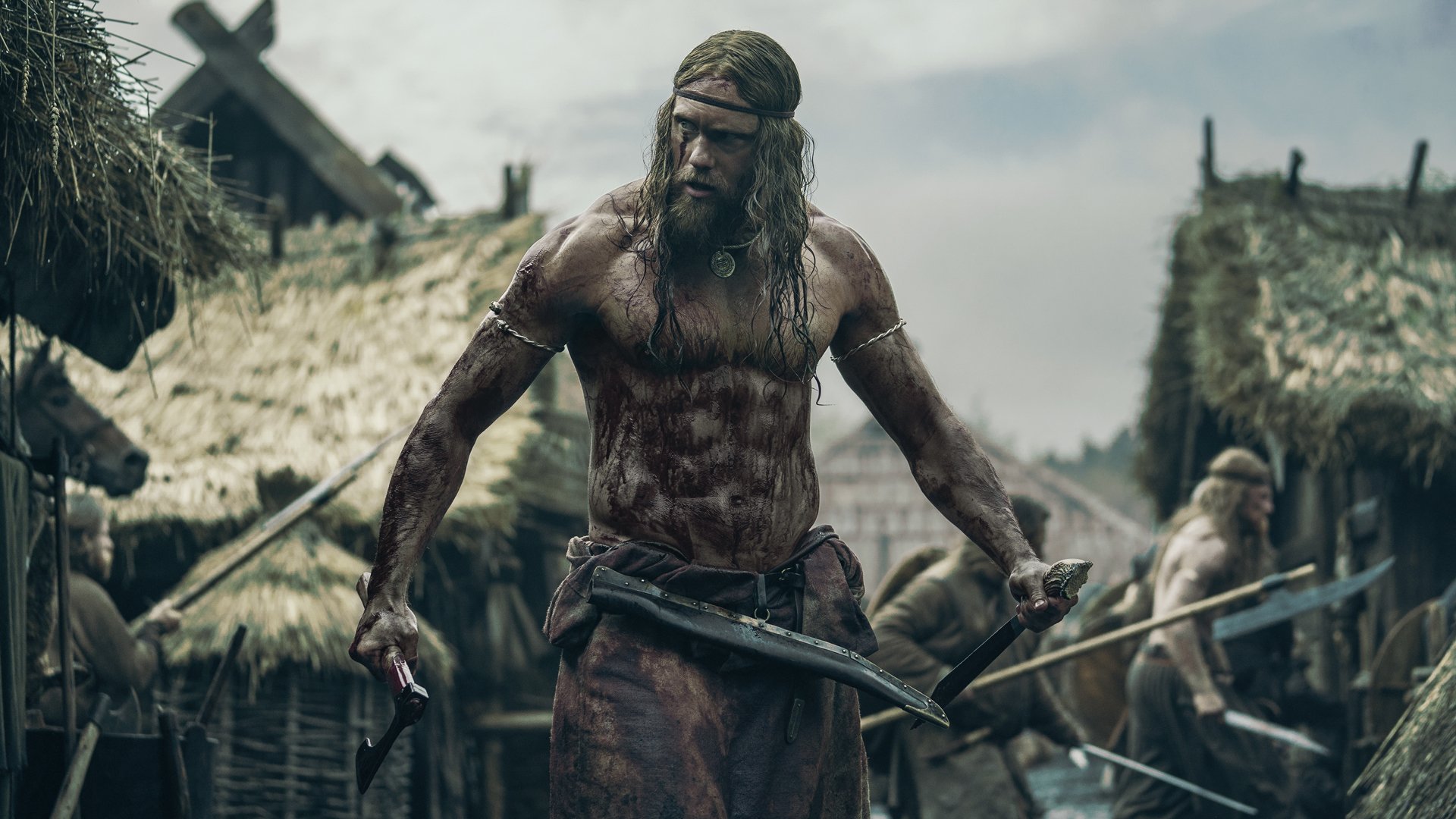 A viking stands in the middle of a village raid, covered in blood.