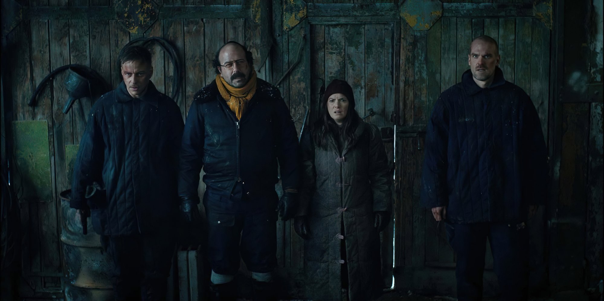Three men and one woman in cold weather clothes stand in a barn.