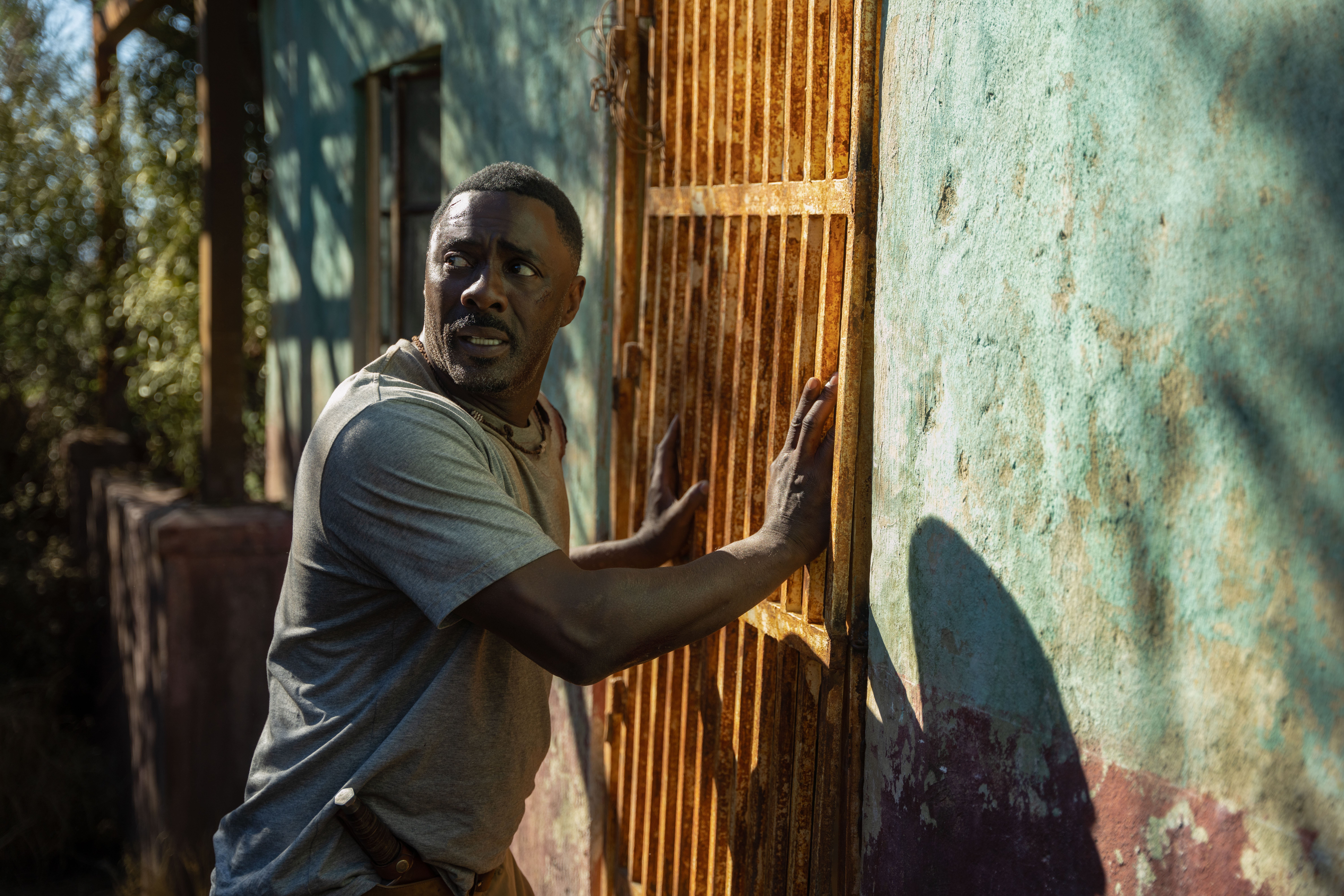 A bloodstained man holds a door closed while looking over his shoulder in fear.