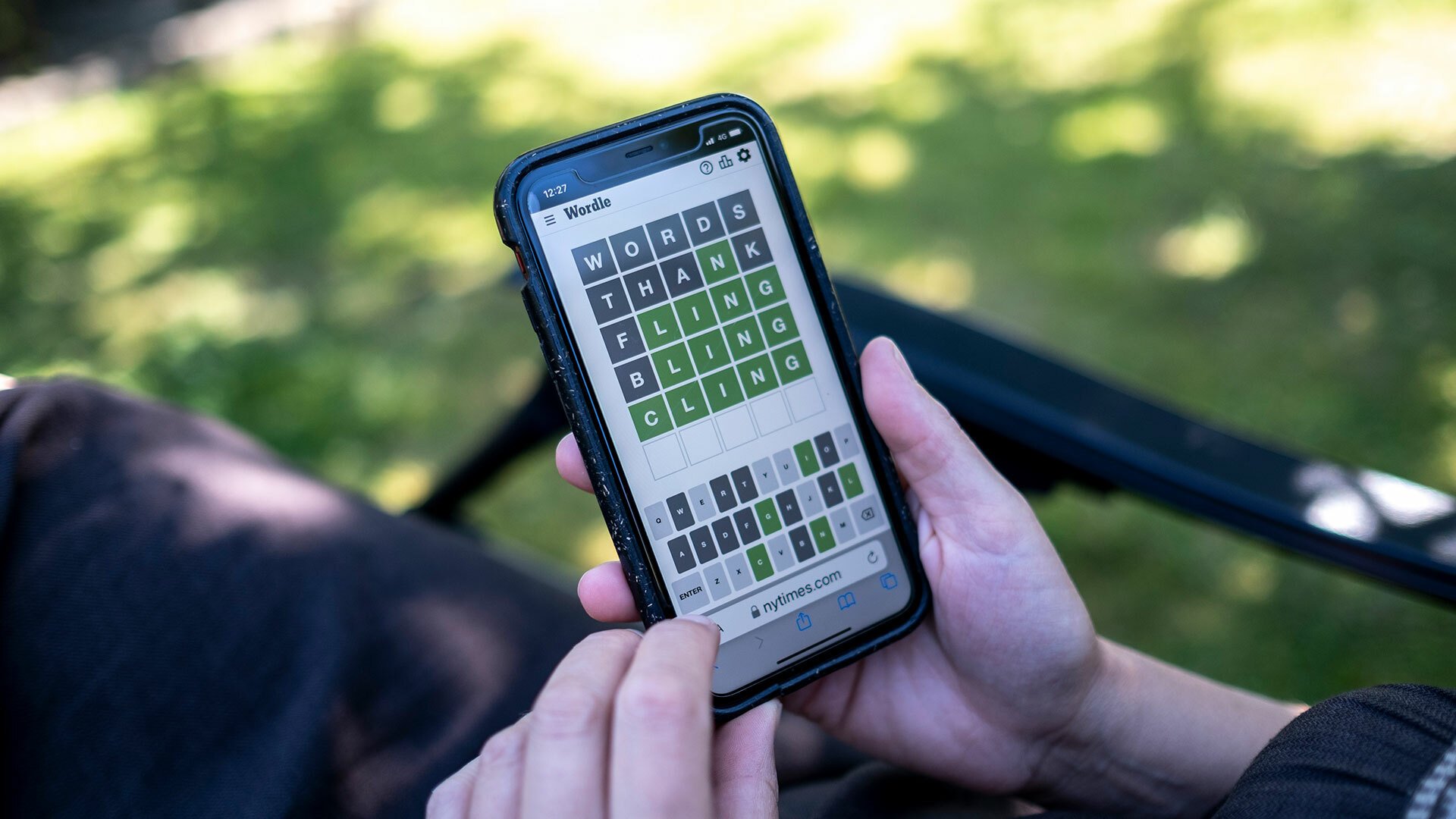 A person sits in their garden playing Wordle on smartphone.