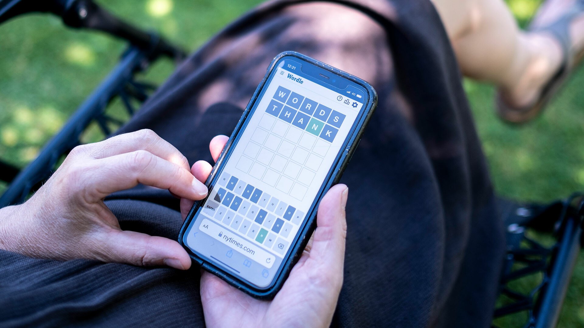 A person sits in their garden playing Wordle on a smartphone.