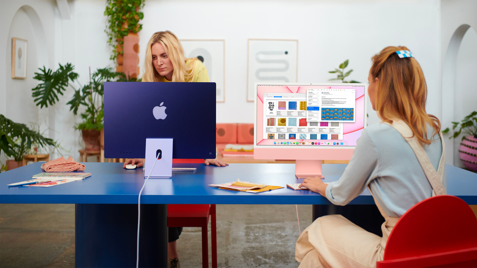 two women working on apple imacs at a blue table in a modern living room