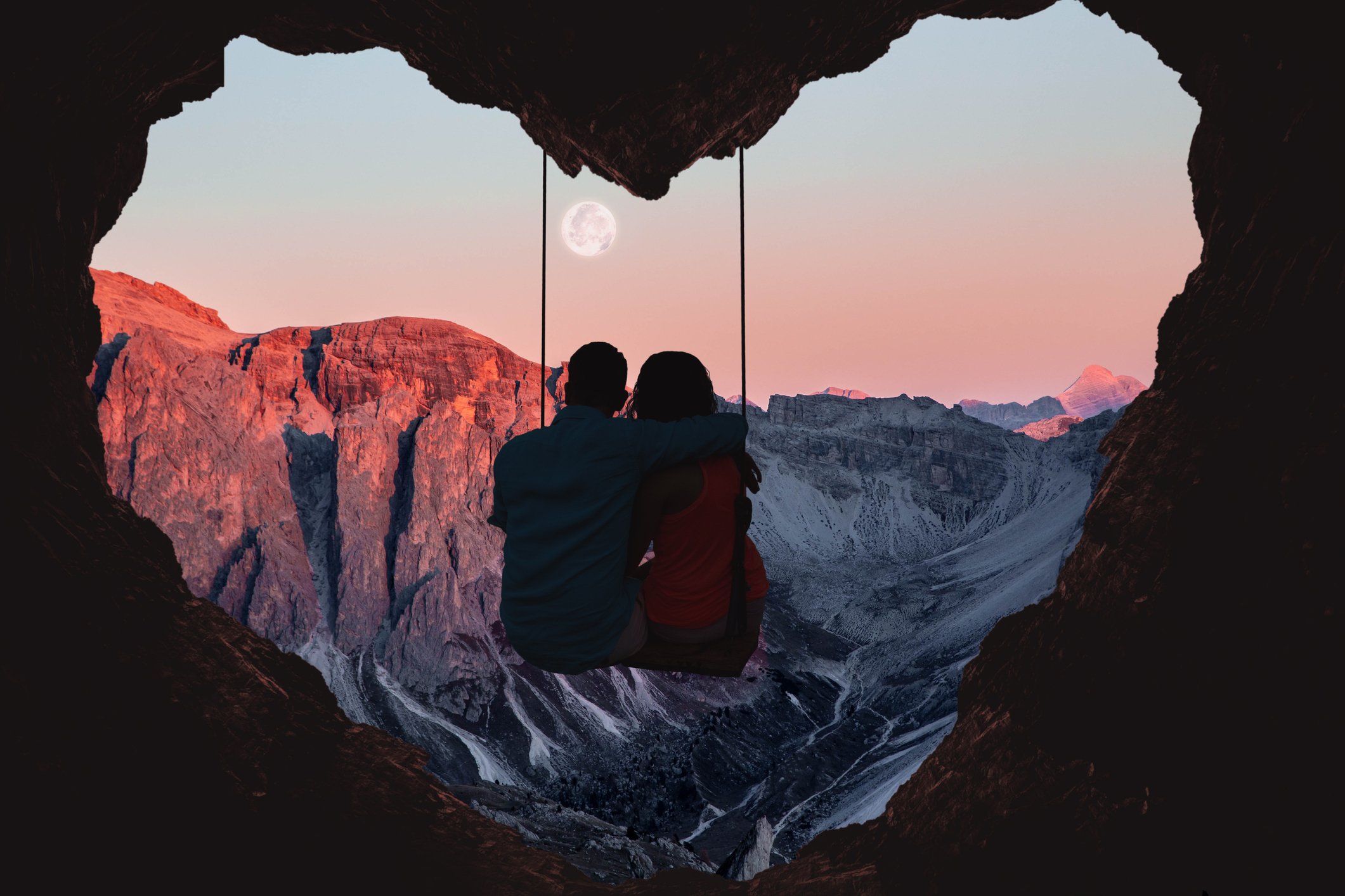 Couple on swing in a heart-shaped cave, looking out at mountains.