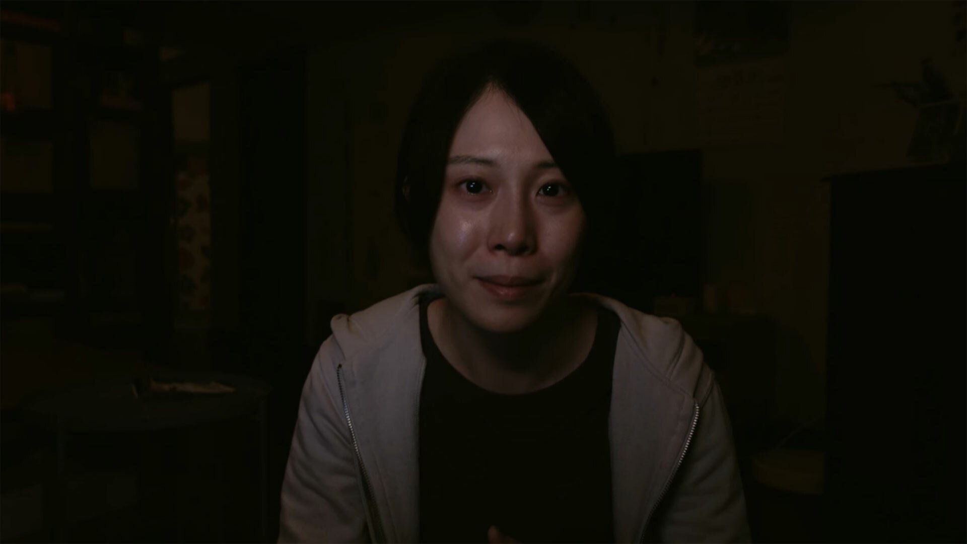 A woman in a dark room looks at the camera.