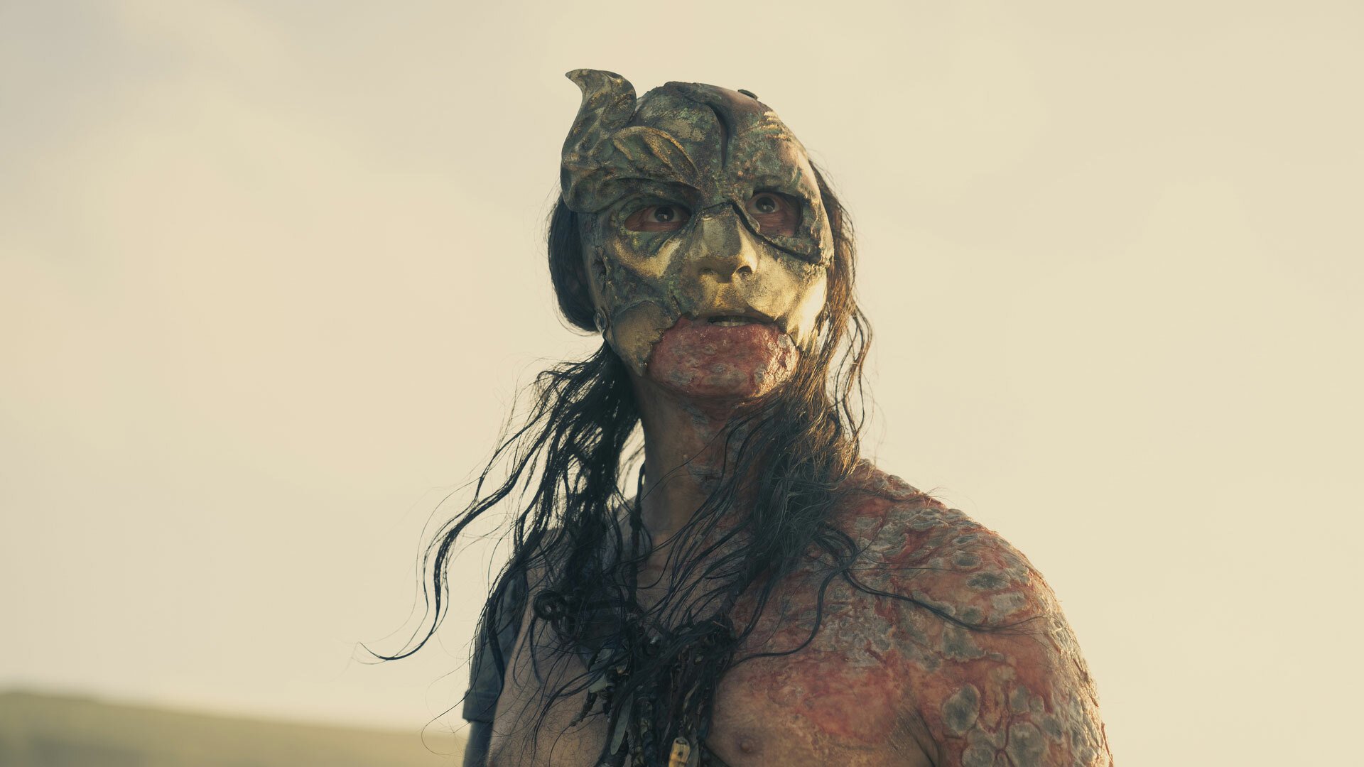 A shirtless man with a mask stands on a beach.