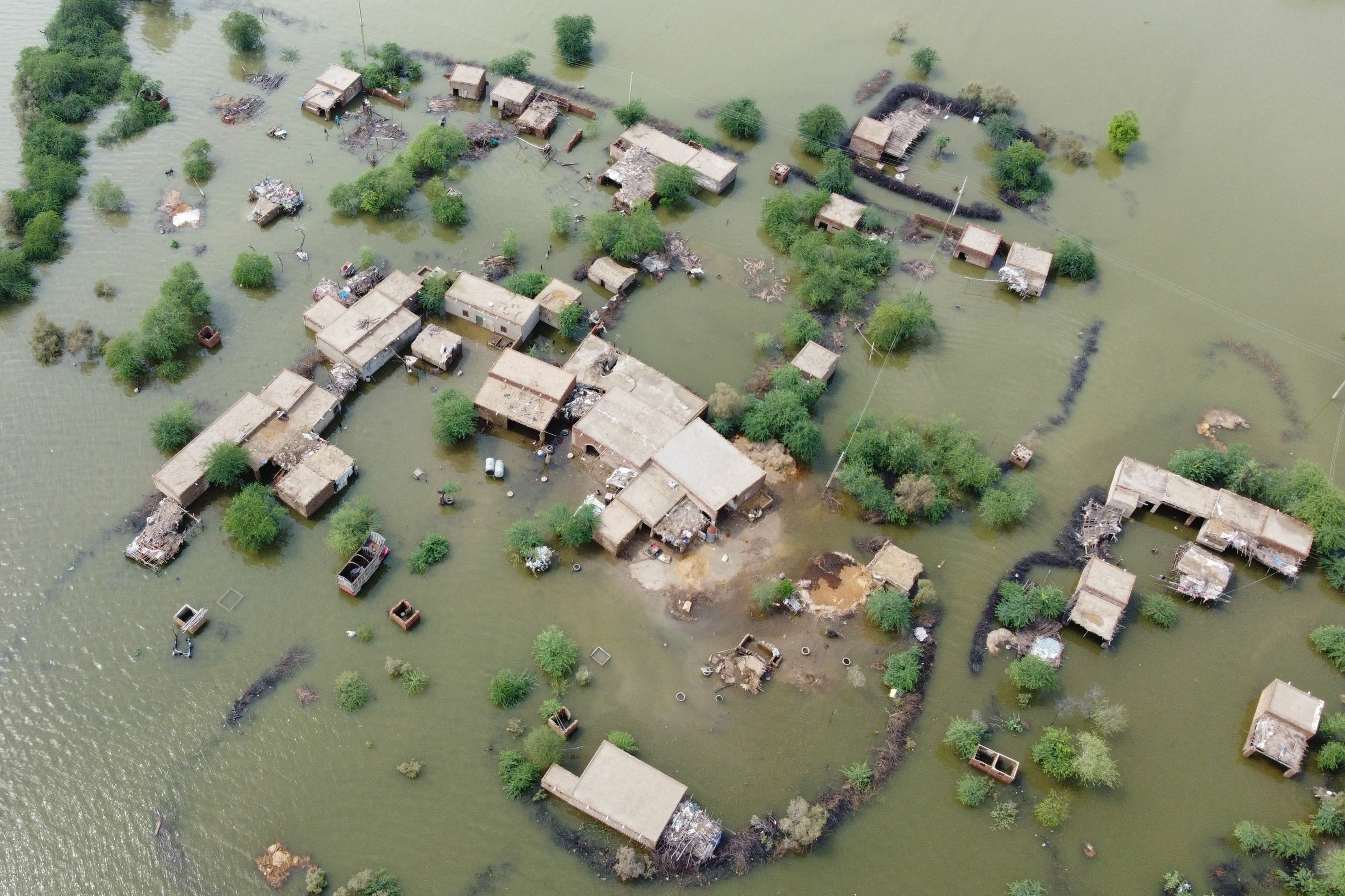 An aerial shot of a flooded residential area. The roofs of houses and the very tops of trees poke out from a green body of water.
