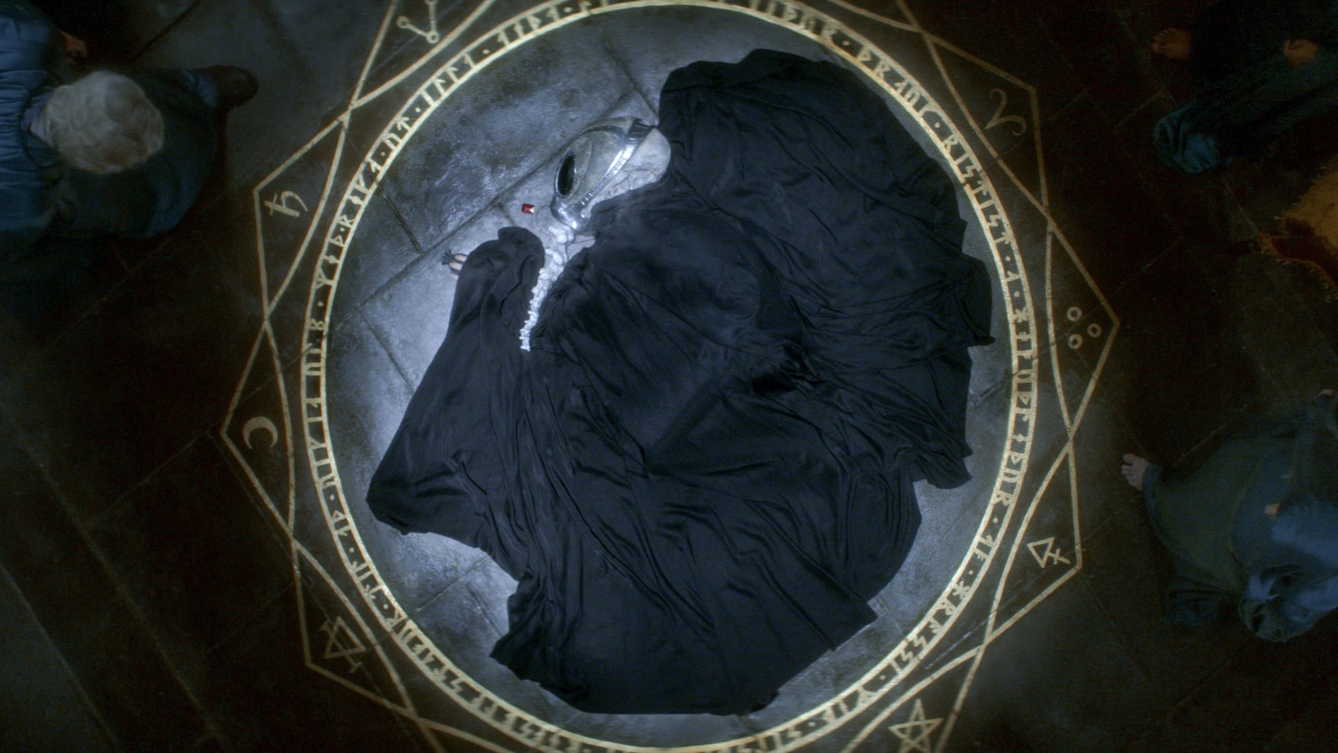 A helmeted figure cloaked in black lies curled up in a gold summoning circle on a stone floor.