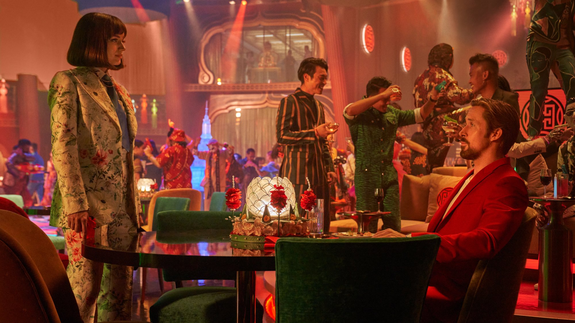 A man and a woman in suits sit in a Bangkok bar staring at each other.