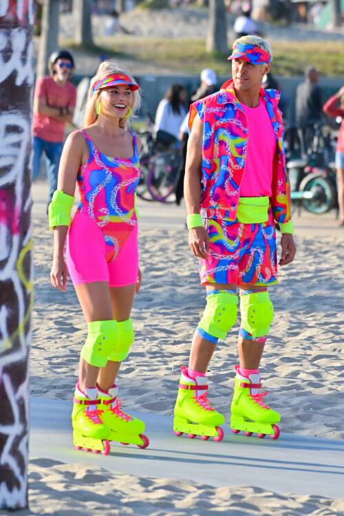 Two people in hot pink and fluorescent yellow leotards and bike shorts wear rollerblades on Venice Beach.