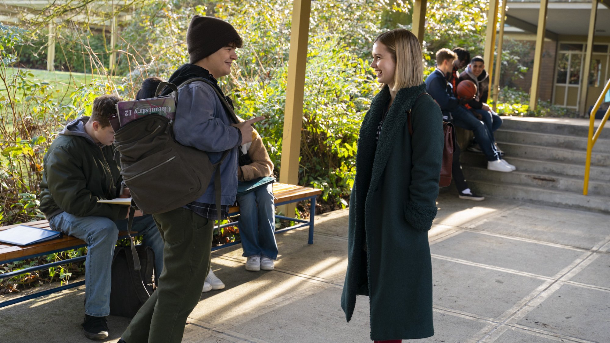 Two teens stand in an outdoor corridoor giggling.