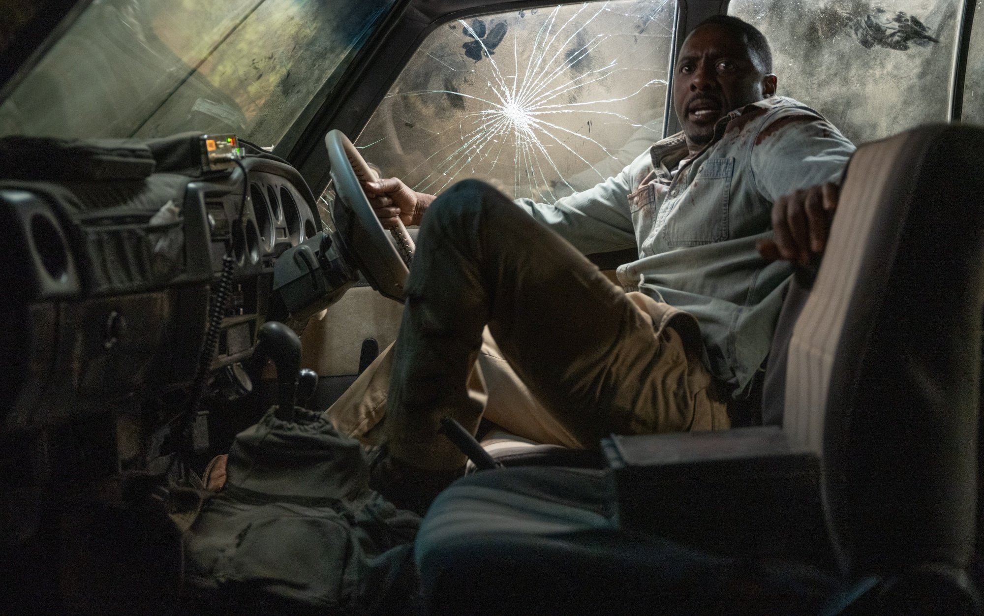 A man in the front seat of a car with a broken window.