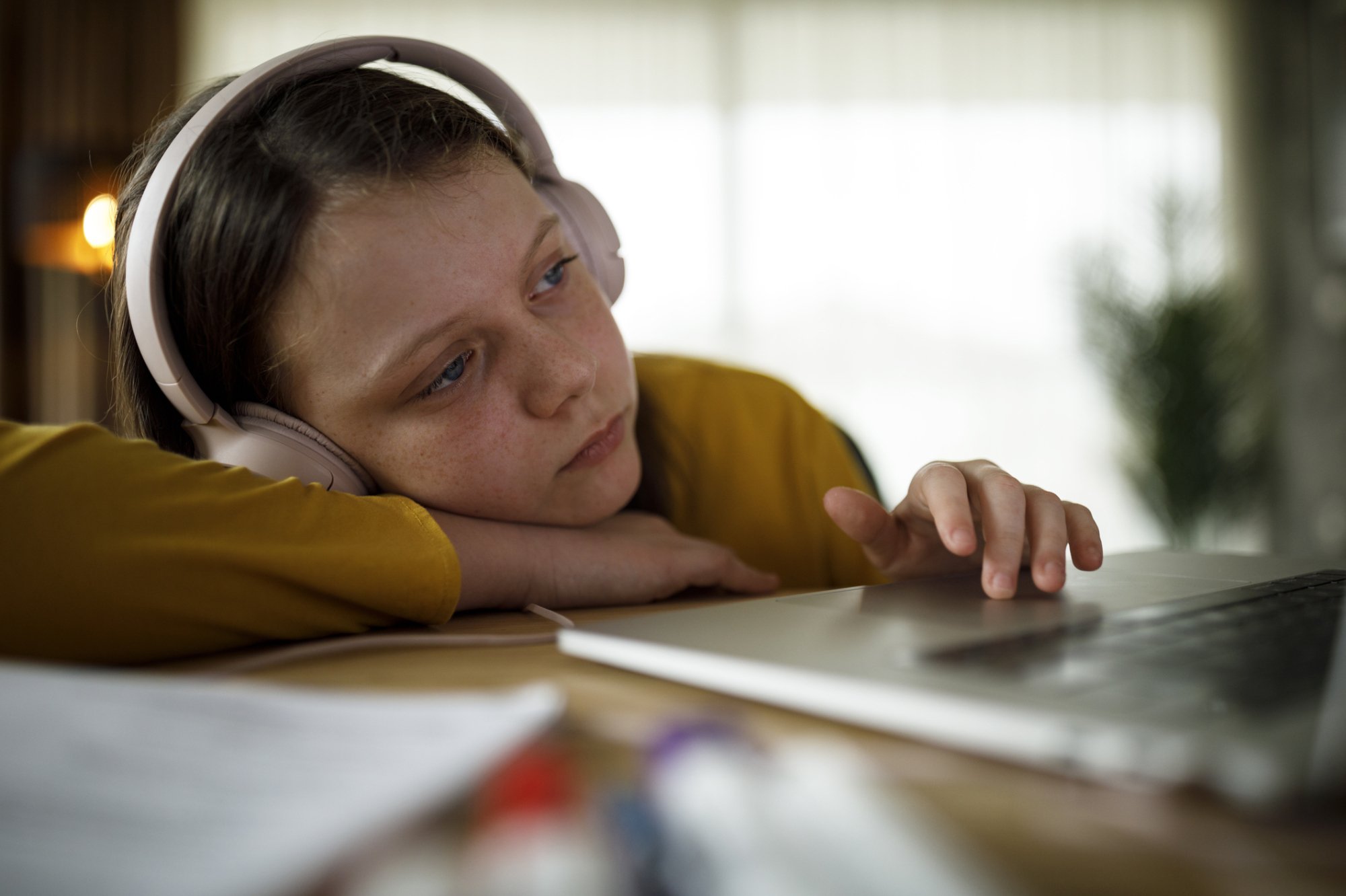 Image of bored girl resting her head on her arm looking at a laptop