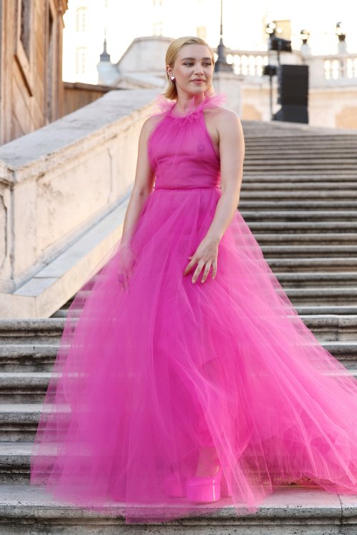 A woman in a bright pink dress stands on an outdoor staircase.