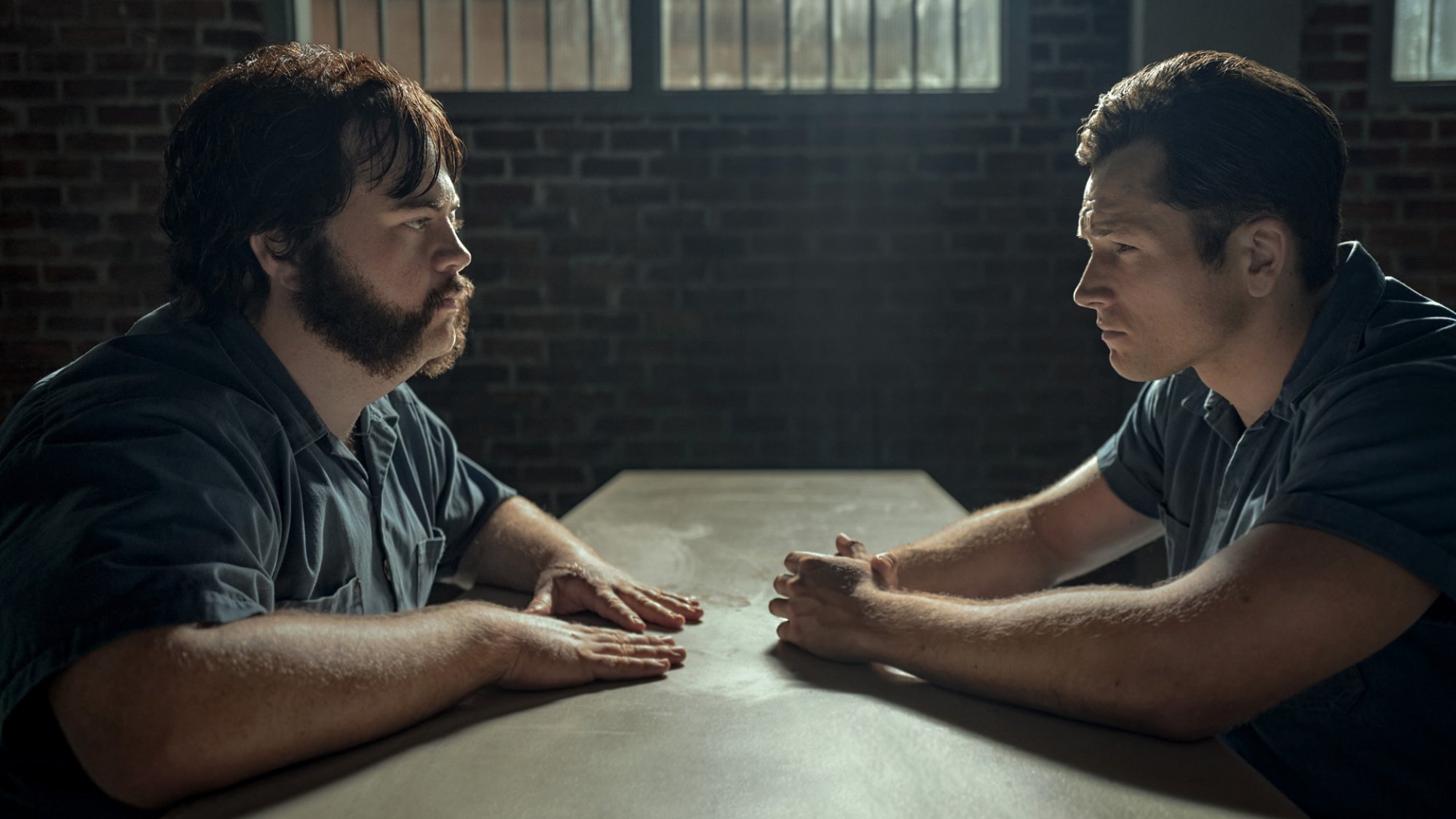 Two prisoners sit across a table from one another.