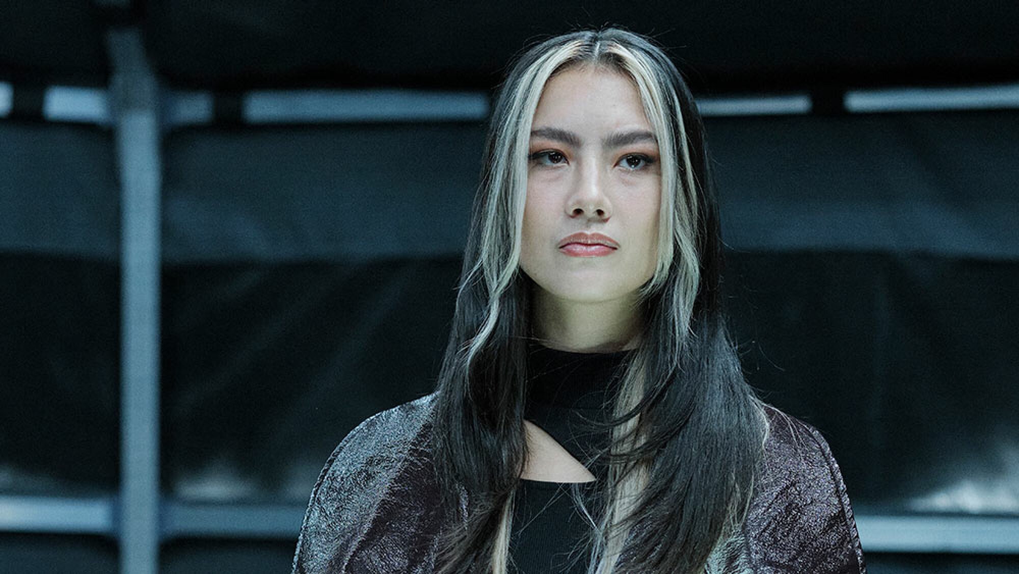 A woman with dark hair and blonde highlights looks serious.