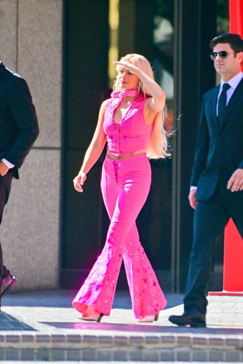 A woman in a bright pink halter neck onesie walks on the street.