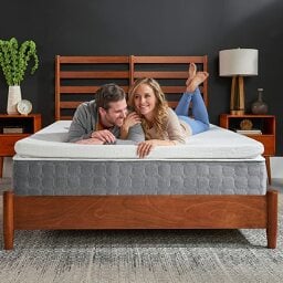man and woman laying on bed with mattress topper