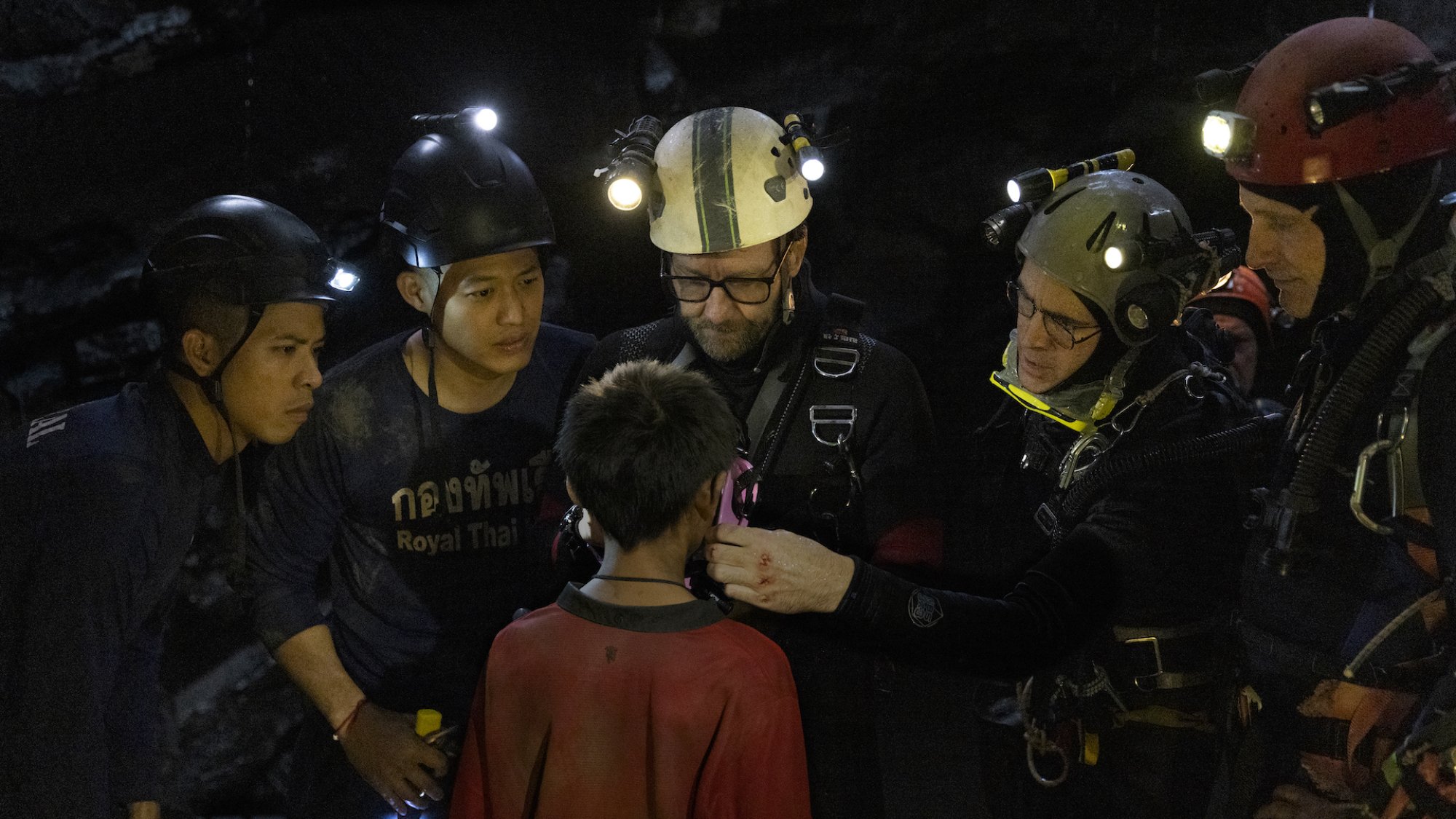 Five divers with headlamps talk to a small boy.