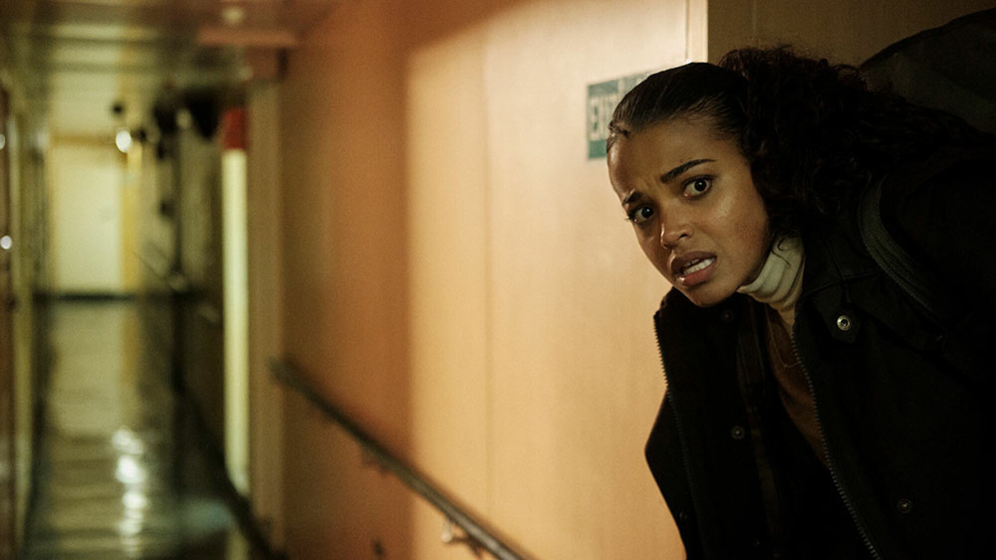 A woman carrying a bag below-deck on a boat peers around a corner.