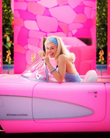 A woman in a bright pink car smiles at the camera.