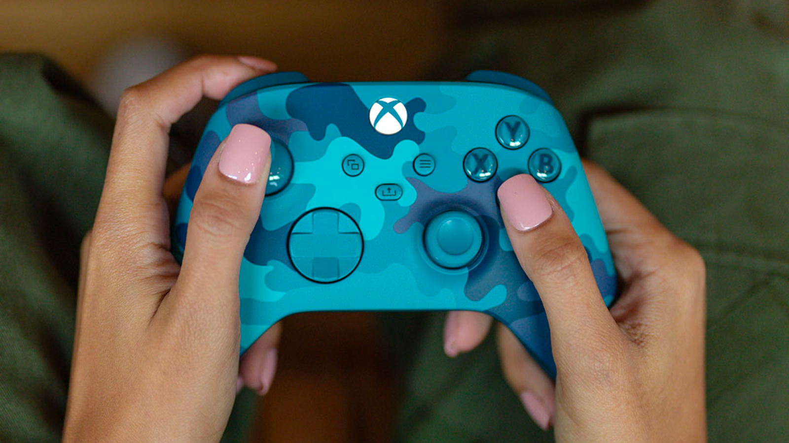 a close-up of a woman with light pink nail polish holding the new Xbox Wireless Controller – Mineral Camo Special Edition
