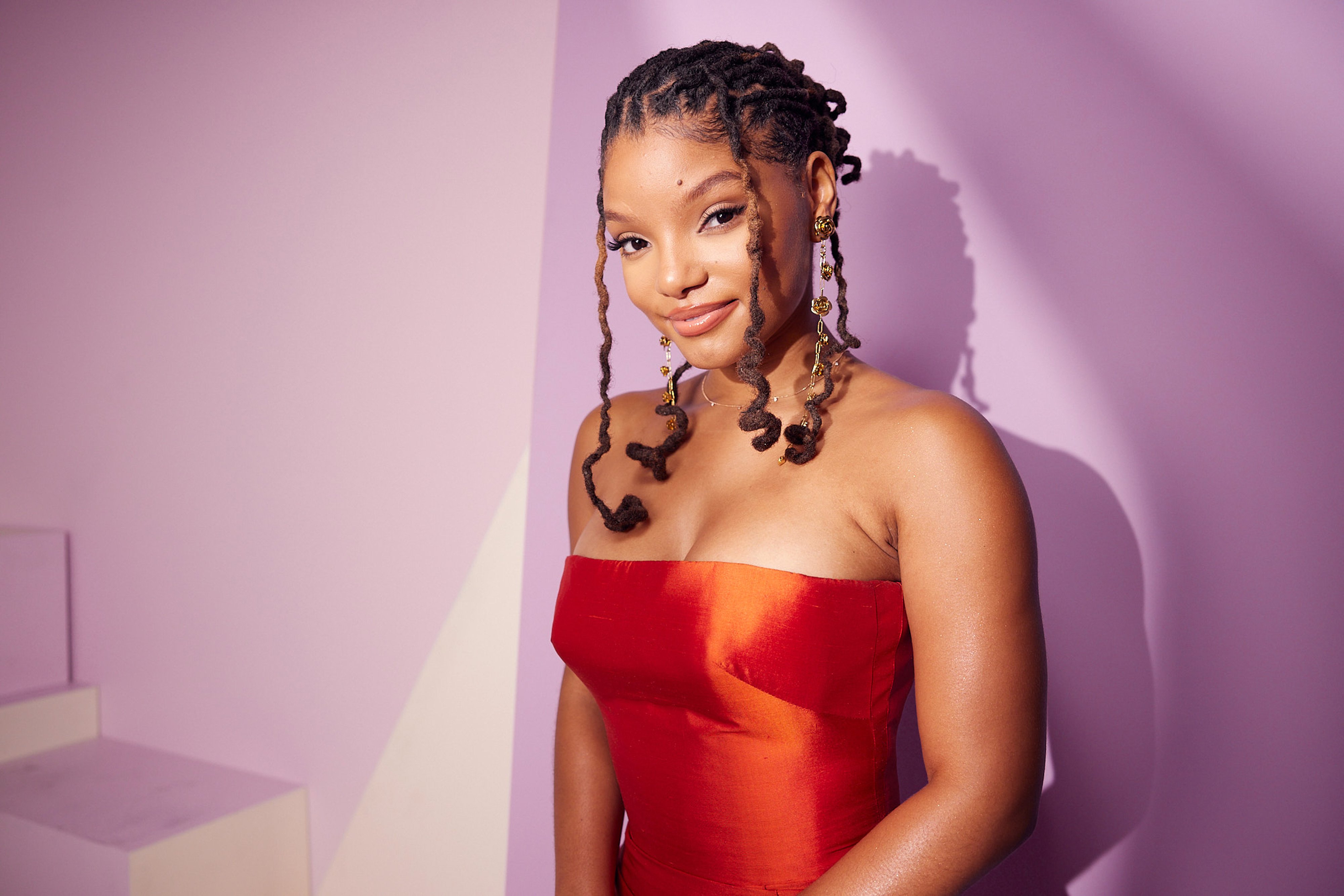 Halle Bailey wearing a red dress in front of a pink background