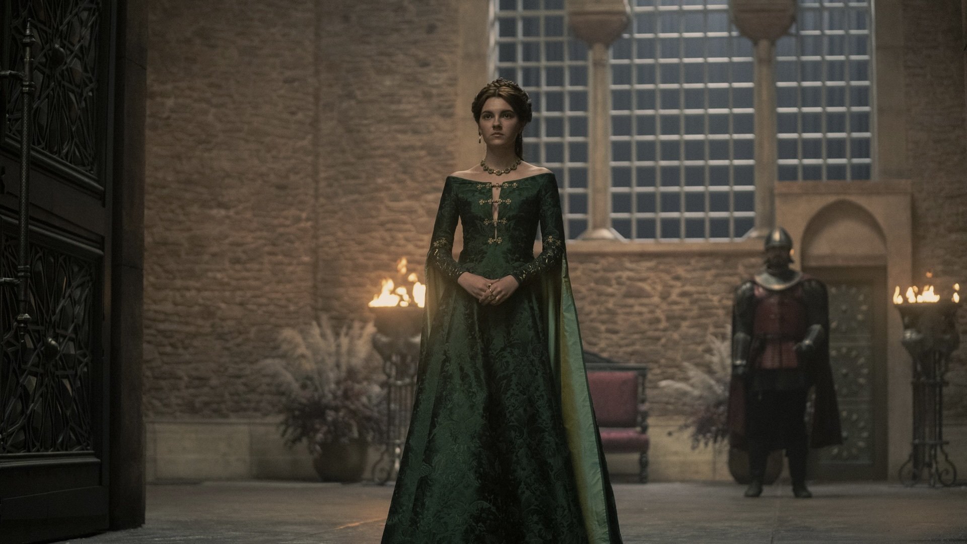 Alicent, a young woman in a lavish green gown, stands at the entrance to a great hall.