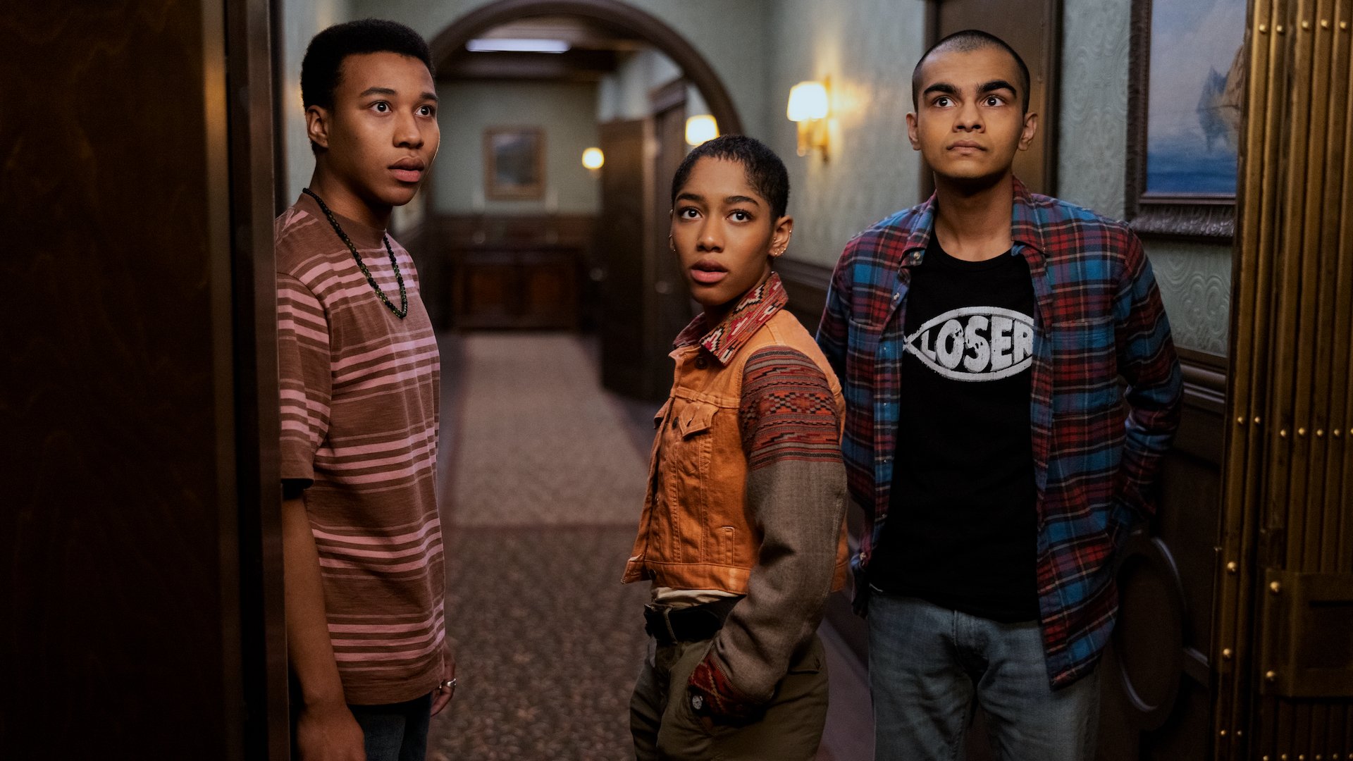 Three teens stand in the hallway of an old house.
