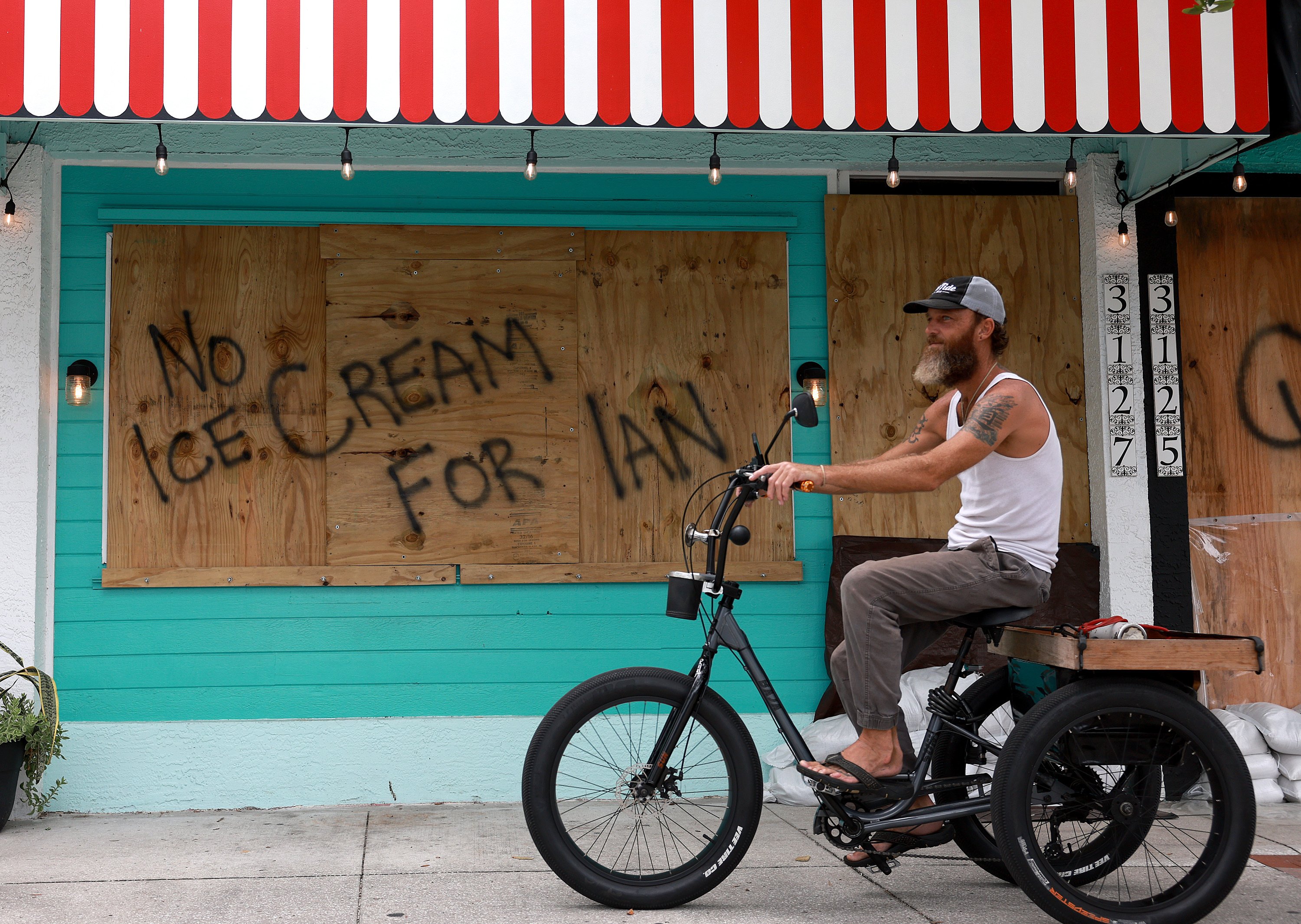 a man rides a bicycle in front of a boarded-up storefront upon which a shopkeeper has spray-painted 