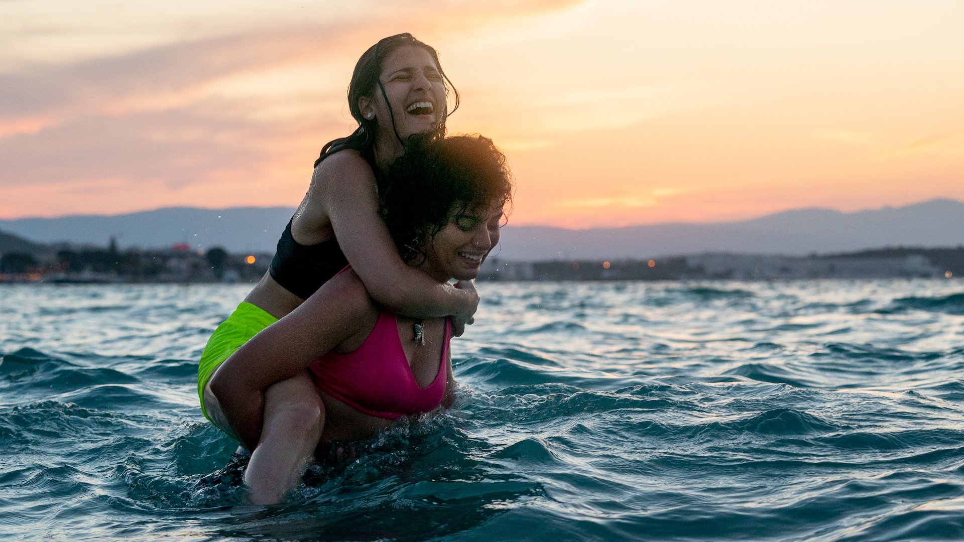 Two young women stand in the sea, one piggybacking on the other.